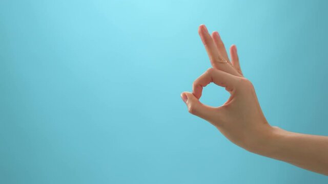 Close up of woman hand showing ok sign okay gesture on the blue background.