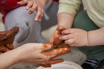 baby hands with clay are guided by an adult.