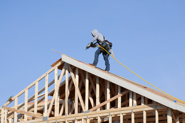 Carpenter using power tool to install roof sheathing during construction of wooden single family home