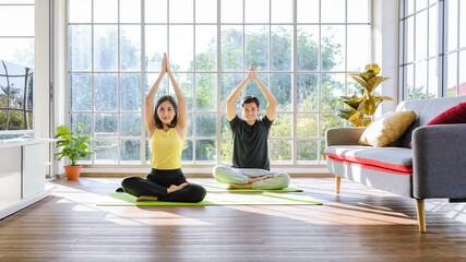 Young Asia couple practicing yoga lesson, breathing and meditating together in living room at home....