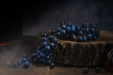 Multiple whole bunches of grapes and grape granules placed on a wooden plate against a dark...