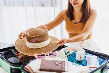 Young woman traveler sitting on the bed packing her suitcase preparing for travel on summer vacation