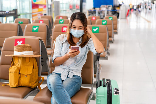Young woman wearing a surgical mask and using mobile phone while waiting for a flight at the airport, New normal lifestyle concept