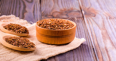 Brown flax seeds or flax seed in a small bowl on sacking and two wooden false on wooden table