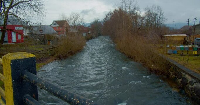 view from a bridge, over a small river in a old village. it's cold, still winter, a gloomy wet day