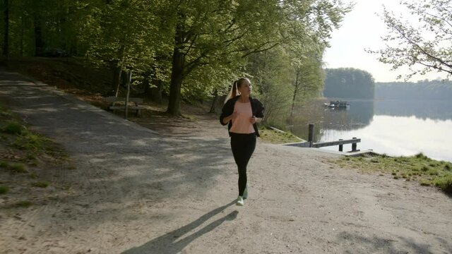 Woman running past lake and woods on sunny day