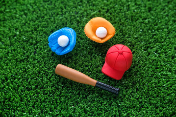 Obraz premium A miniature toy baseball equipment of cap,ball,glove and bat on green grass background. 