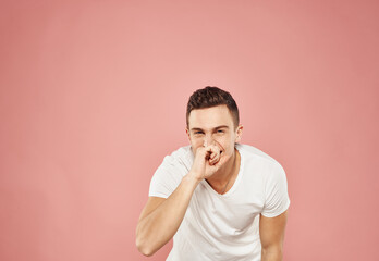 A man gestures with his hands in a white t-shirt emotions pink background