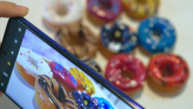 They hold a smartphone in their hands and take pictures of the spread out multi-colored donuts, sprinkled with colored sprinkles, donuts lie in three rows. Close-up. Photo concept for social networks.