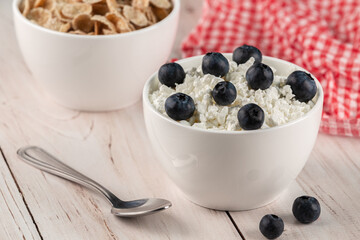 Fresh cottage cheese with blueberries and flakes on a white wooden background with a red checkered napkin