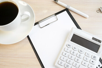 A stationery tablet with a white calculator on a wooden table near a white coffee cup. Business concept. Template.