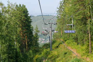 Chairlift in the mountains. Cable car supports. Summer season, green trees, grass. Summer mountain resort concept.