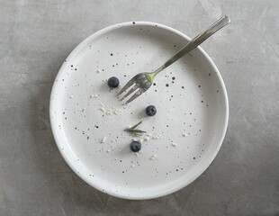 Top view of round white ceramic plate with fork, Dirty dishe after eating blueberry cheese pie is finished on  concrete in coffee cafe.
