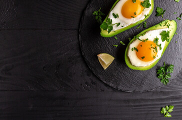Avocado baked with eggs, fresh parsley on black background, banner, menu recipe place for text, top view
