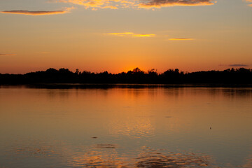 Naklejka premium A colorful sunny sunset is reflected on the surface of the calm lake.
