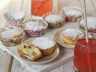 Freshly baked homemade raisin muffins in paper tins on a wooden background with raspberry juice.