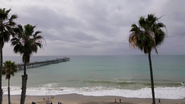 An aerial drone shot flying over San Clemente State Beach, California, towards the San Clemente Pier on a cloudy day.