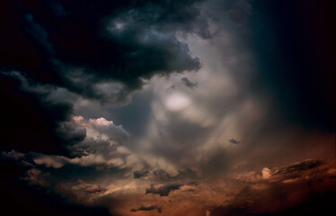 Dramatic turbulent clouds from an approaching storm front brightly lit by the light of the setting sun through an opening in the clouds producing a shape resembling a man's face getting ready to blow.