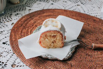 Slice of a lemon cake with sugar frosting in a ceramic plate, fork, lemons on rustic wooden background.