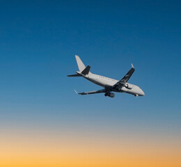 Fototapeta na wymiar Close up of large passenger airplane flying in beautiful blue and orange sunset sky.