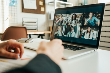 Woman has video call with her teammates using laptop.  White loft workspace. Close-up