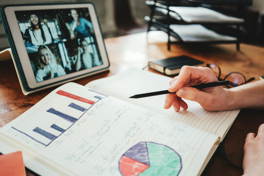 Woman has video conference call with her remote teammates using tablet computer. Note pad with stats close-up