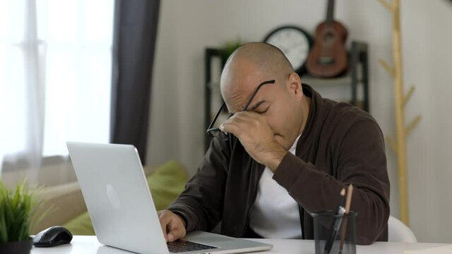 Tired businessman working with laptop. He covered his mouth with his hand and yawned. He is very sleepy and take off glasses. He work from home.

