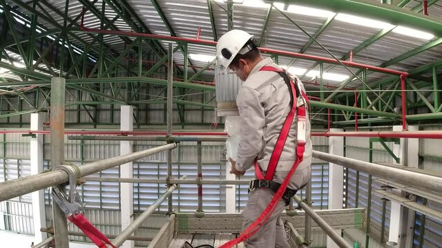 An electrician is working on a steel scaffold to fix the light bulb, wearing safety equipment to prevent falling from a height. 
