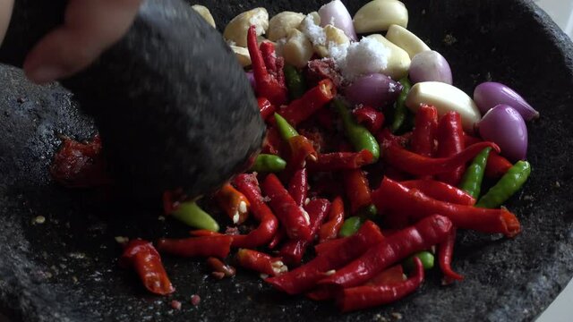 hand pounding red and green chilies, garlic and onion in stone mortar, chef preparing Indonesian traditional spicy hot chili sauce