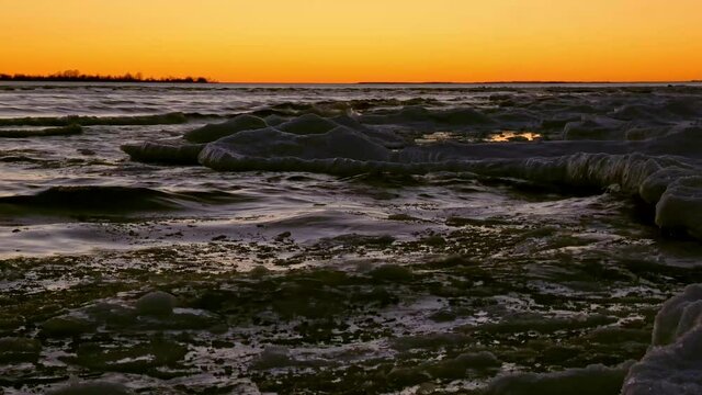Along the edge of a frozen shoreline, waves lap against the winter ice pack.