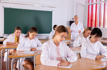 Medical students doing test in college, writing in notepads during lesson