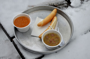 soup on an aluminum tray in a polystyrene bowl with plastic cutlery and a croissant on a wooden...