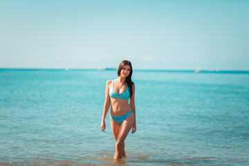 Fototapeta na wymiar Summer. A young pretty woman poses standing at the ocean. The concept of summer holidays. Copy space
