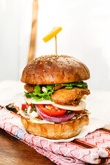 Burger z kurczakiem na jasnym tle, drewnianym stole w świetle dziennym.