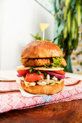 Burger z kurczakiem na jasnym tle, drewnianym stole w świetle dziennym.