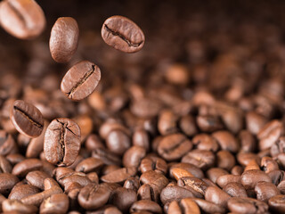 Several roasted coffee beans fall down towards the coffee beans. Horizontal photo.