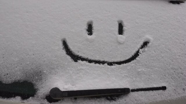 Snow background. Texture of wet snow with a cheerful smiley symbol pattern in the winter window of the car outdoors close-up. Smile in the snow, happy cheerful image. Winter time concept.