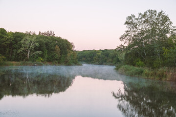 Fototapeta na wymiar Fog above the river surface on a summer calm morning, trees reflected in the water. Silence and natural beauty. Nature. Landscape - Foggy river