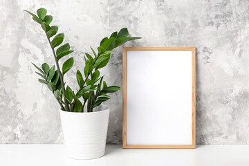 Wooden vertical frame with white blank card, and green houseplant flower in pot on table on gray concrete wall background. Mockup Template for your design, text