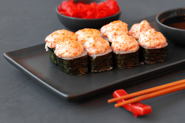 Baked sushi roll served on black plate on wooden table