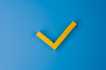Check mark, tick and yes symbol made with yellow wooden blocks on blue background