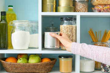 Woman taking metal can from shelves with products in kitchen