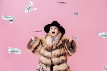 Playful little boy in oversized luxurious fur coat and classical hat making rock'n roll gesture...