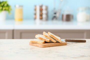 Board with toasts and knife on table in modern kitchen