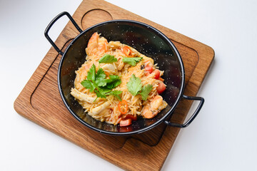 Seafood fried rice with shrimps and vegetables. Served in a black wok pan over white background.