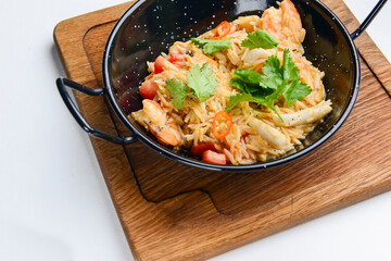 Seafood fried rice with shrimps and vegetables. Served in a black wok pan over white background.