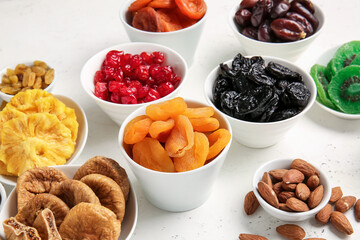 Bowls with different dried fruits and nuts on light background