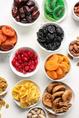 Bowls with different dried fruits and nuts on light background
