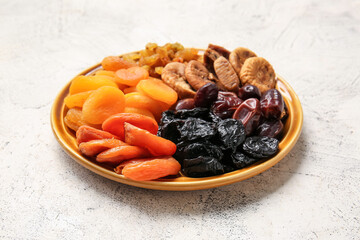 Plate with different dried fruits on light background