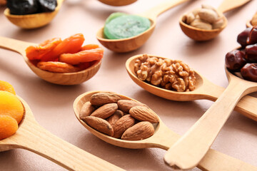 Spoons with different dried fruits and nuts on color background